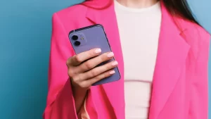 Mulher vestida com blazer rosa e segurando um celular