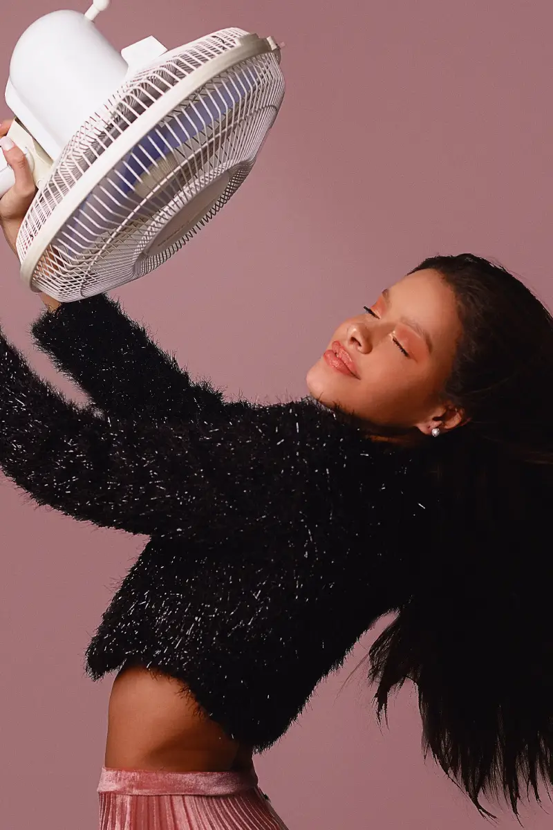 Mulher segurando um ventilador diante do rosto por causa da sensibilidade ao calor